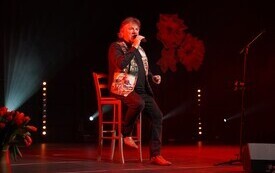 Mariusz Kalaga siedzący na krześle pośrodku sceny podczas koncertu z okazji Dnia Kobiet w M-GOK w Osieku. 