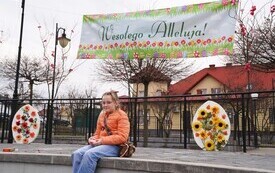 Dziewczynka siedząca na murku za nią dekoracje świąteczne na rynku w Osieku. 