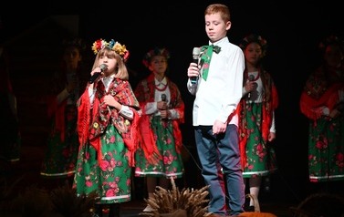Od lewej podopieczna MGOK śpiewająca piosenkę podczas spektaklu obok niej stoi chłopiec. Oboje ubrani są w stroje w klimacie ludowym. 